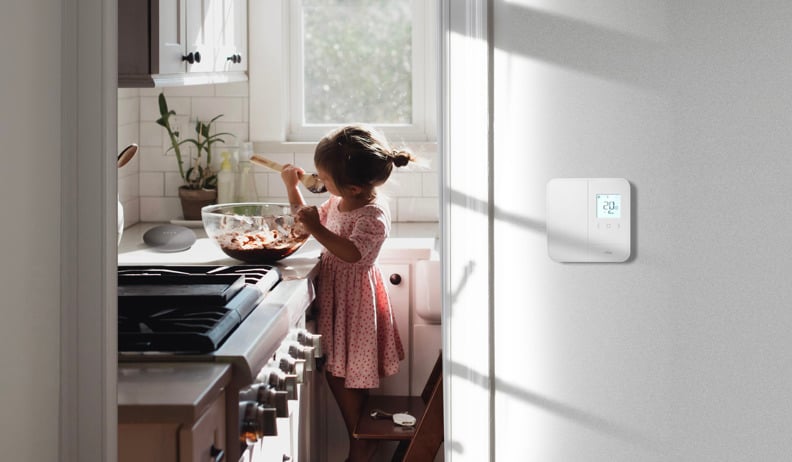 Petite fille sur un escabeau mélangeant du chocolat dans un bol dans une cuisine lumineuse; un thermostat mural affiche 20 °C.