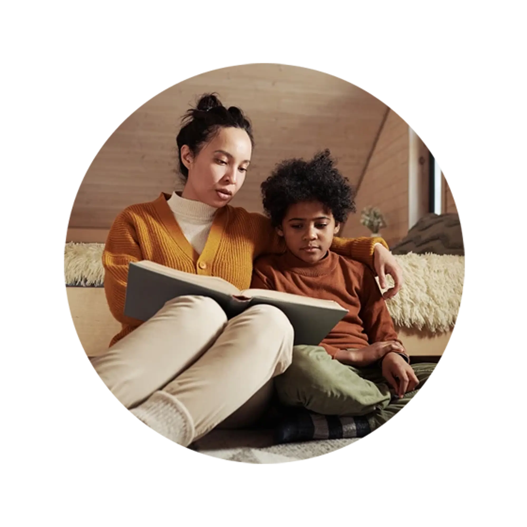 A mother and her son sitting on a sofa, reading a book together in a cozy wooden interior.
