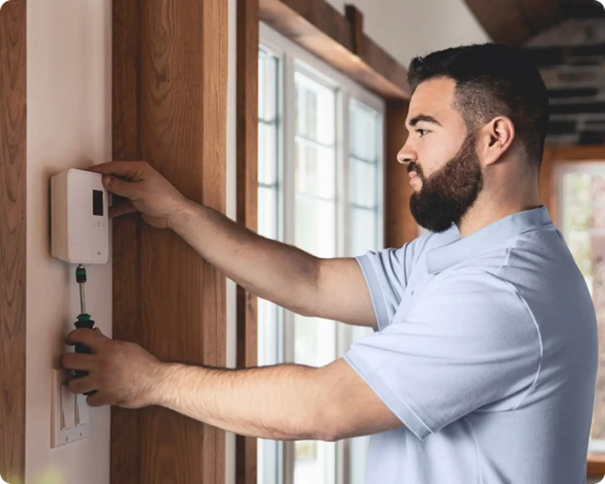 Technicien Hilo installant un thermostat intelligent à l’intérieur d’une maison, utilisant un tournevis pour fixer l’appareil.