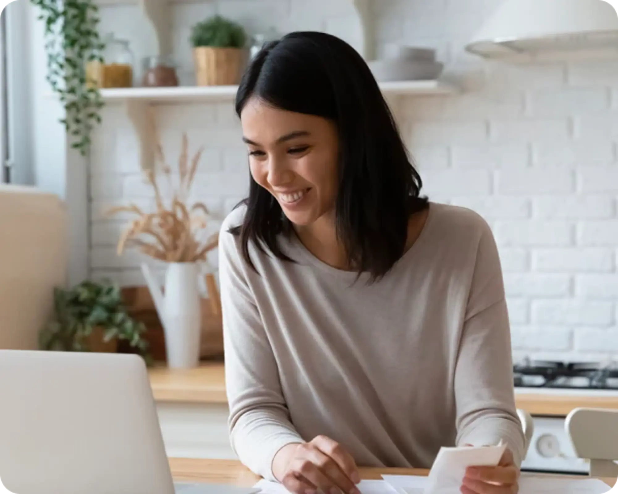 Woman working on a laptop at a table in a bright kitchen.