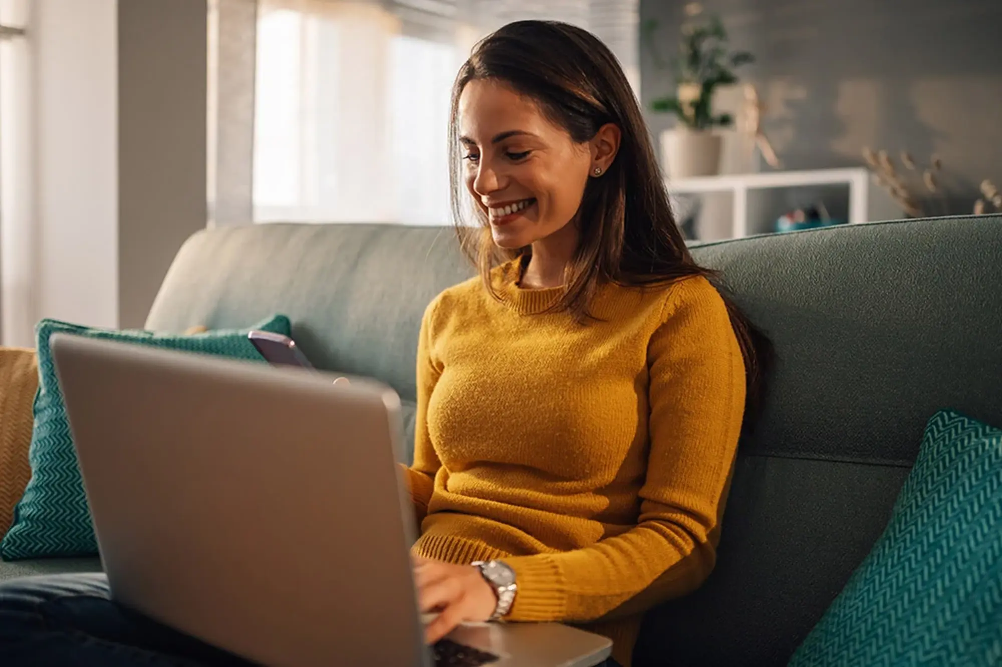 Femme assise sur un canapé utilisant un ordinateur portable dans un salon moderne, dans une ambiance chaleureuse.