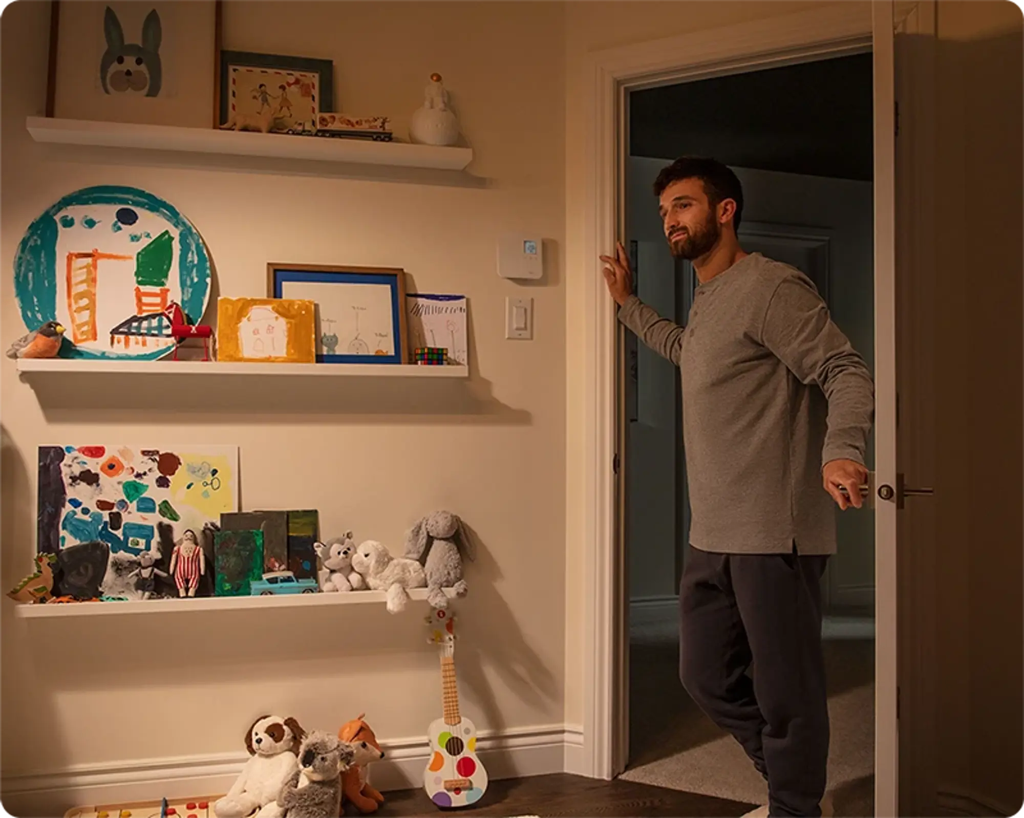 A father standing near an open door, adjusting a wall thermostat in a child's bedroom.